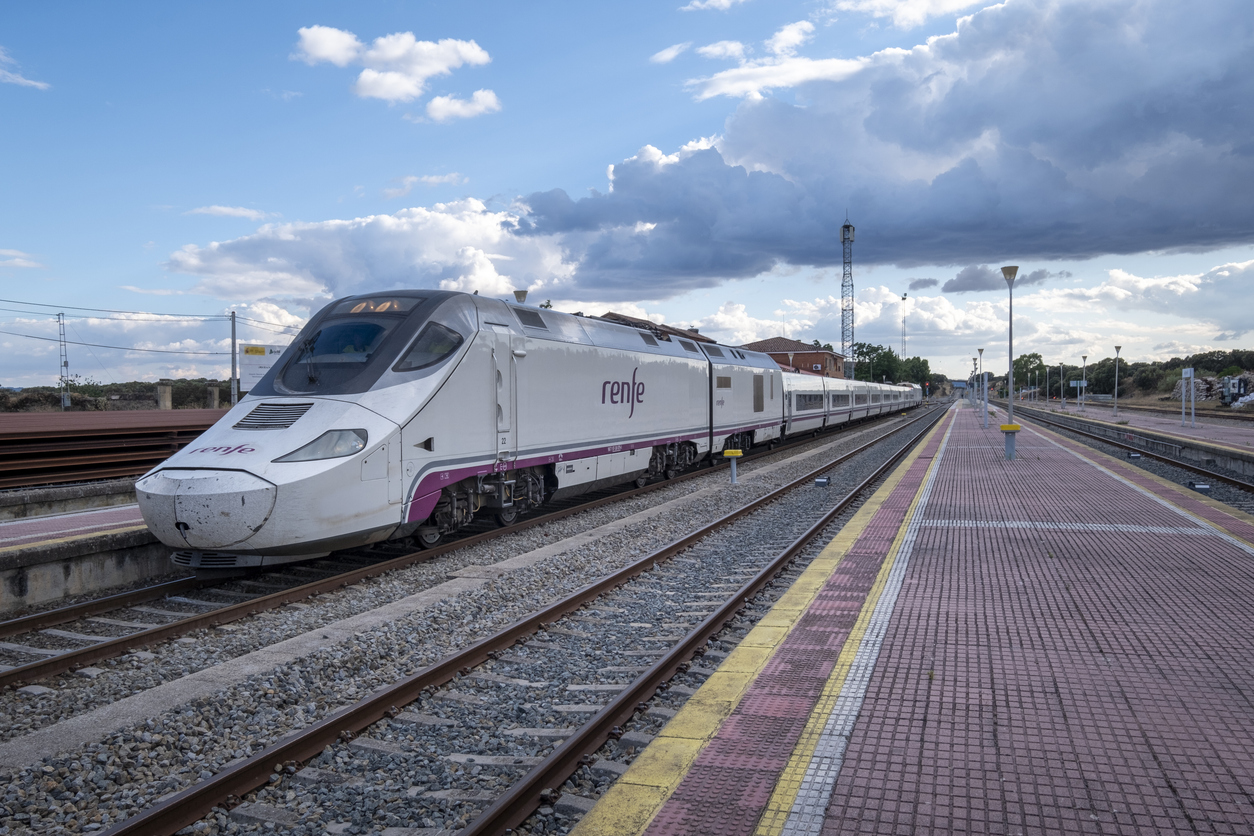 A modern train stopped at the old and still functioning Monfrague or Palazuelo Empalme train station. How to book a train in Spain using Trainline vs Omio, comparing whether Omio train is reliable and if Trainline or Omio is better for Spanish rail travel